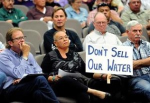 Merced County resident Rose Marie Burroughs made her position clear by holding a sign at the County Supervisors meeting on Tuesday, May 20, 2014. Seated next to her left is Stephen Smith of the Turlock Fruit Co. who stands to make millions from the groundwater sale.